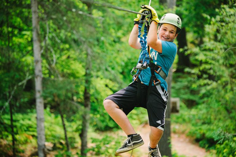 jeune garçon souriant et s'amusant sur une tyrolienne dans la forêt